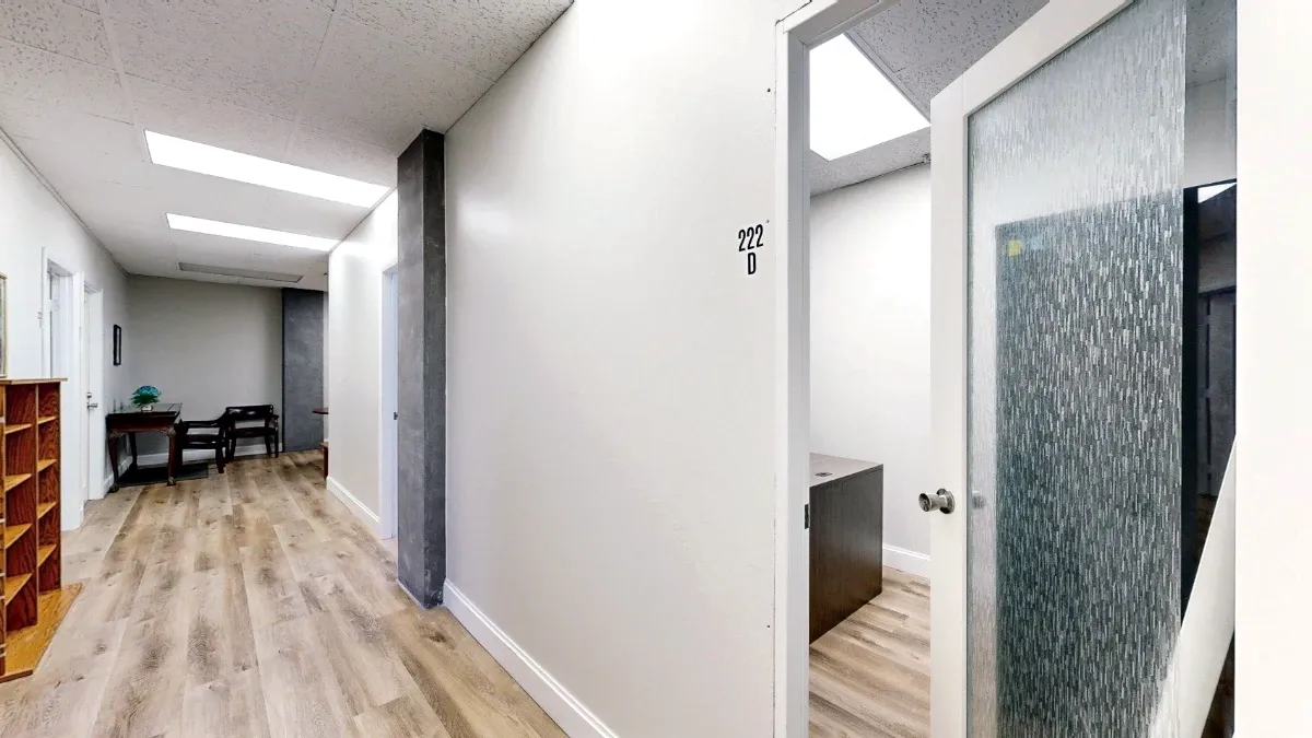 View down Suite 222's hallway with office D's glass door in the foreground, wooden cubbies left, and seating beyond.