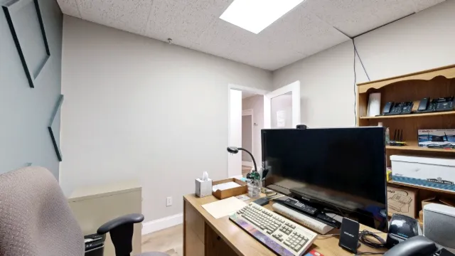 A close view of Office 209's monitor and keyboard, with an upholstered chair, open doorway and wooden shelving behind.