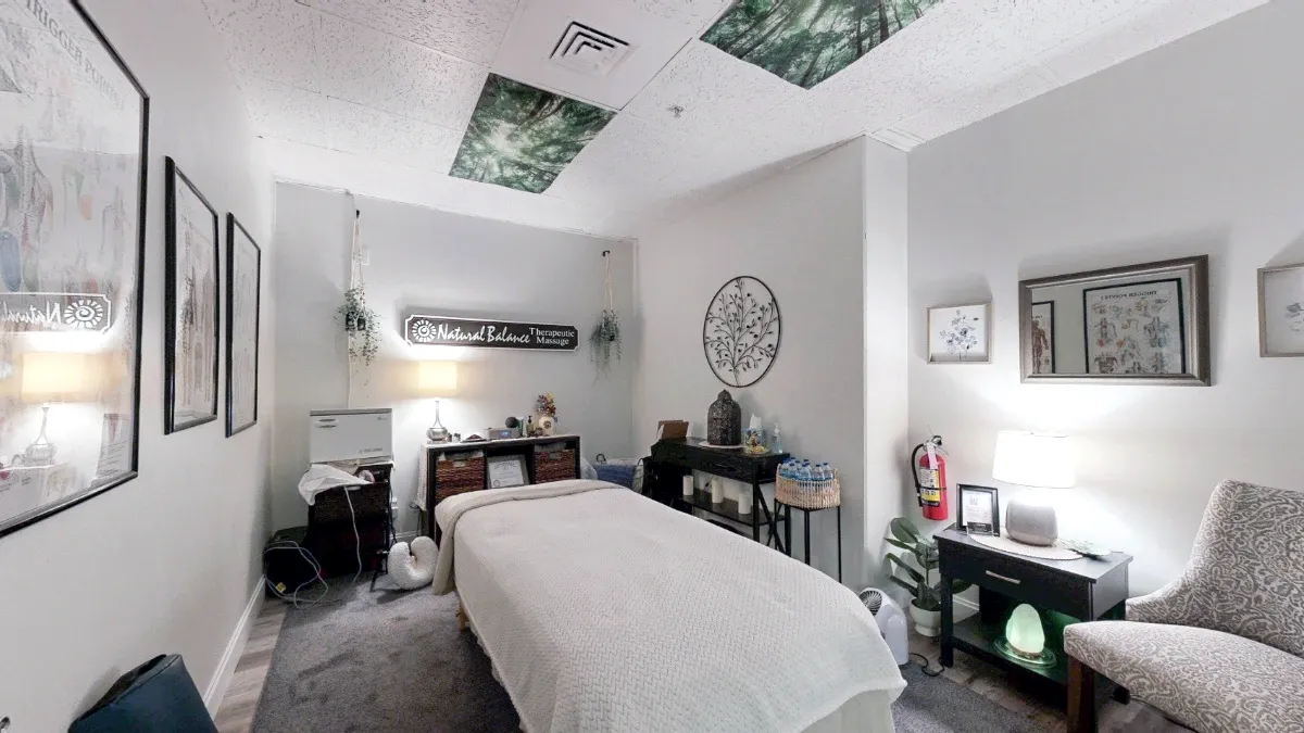 A covered massage table fills Office 219, surrounded by lamps, storage shelves, a patterned chair and forest-print ceiling panels.