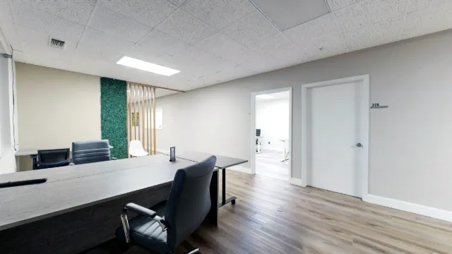 Shared desks and black office chairs in an open coworking area with wood-look flooring and a green accent divider.