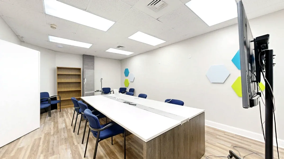 View along The Canaveral's white meeting table toward a wooden bookshelf, with blue chairs and a display in the foreground.