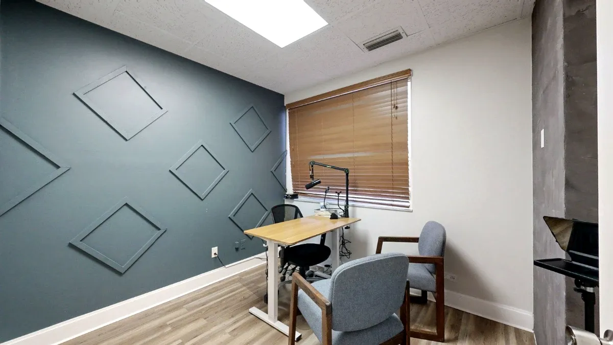A wood-top desk and two gray guest chairs sit beside a blue-gray wall with diamond-shaped trim.