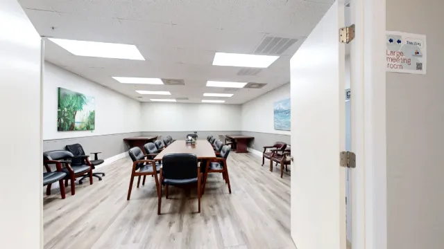 Open doorway framing a long conference table, padded chairs and wall art, with a large meeting room sign at right.
