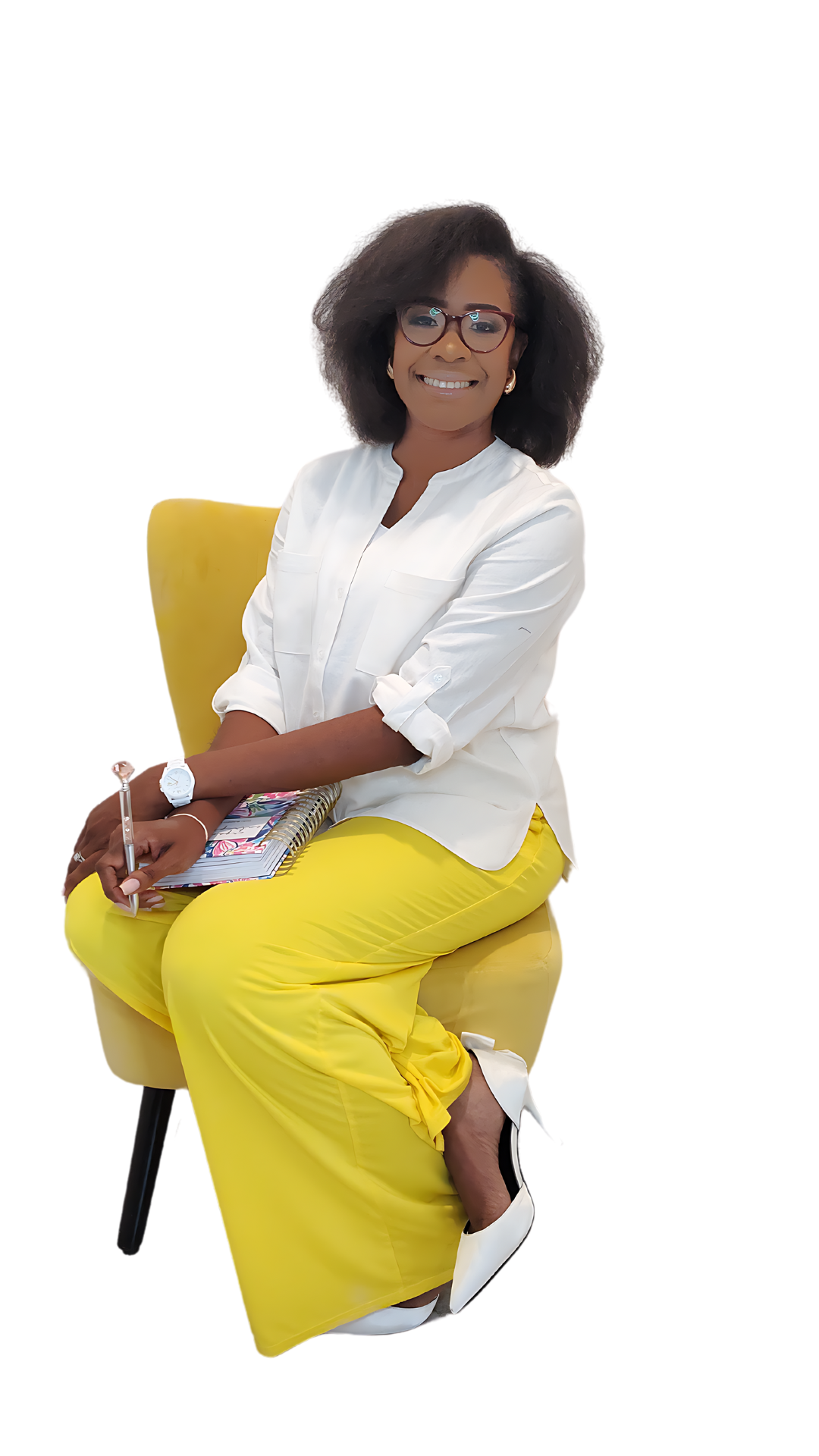 A smiling woman in glasses, a white blouse and yellow trousers sits on a yellow chair holding a notebook and pen.