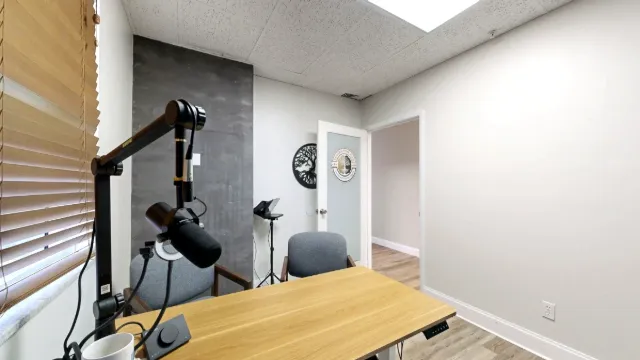 A microphone on an articulated arm hangs over the wood desktop, with guest chairs and the open doorway beyond.