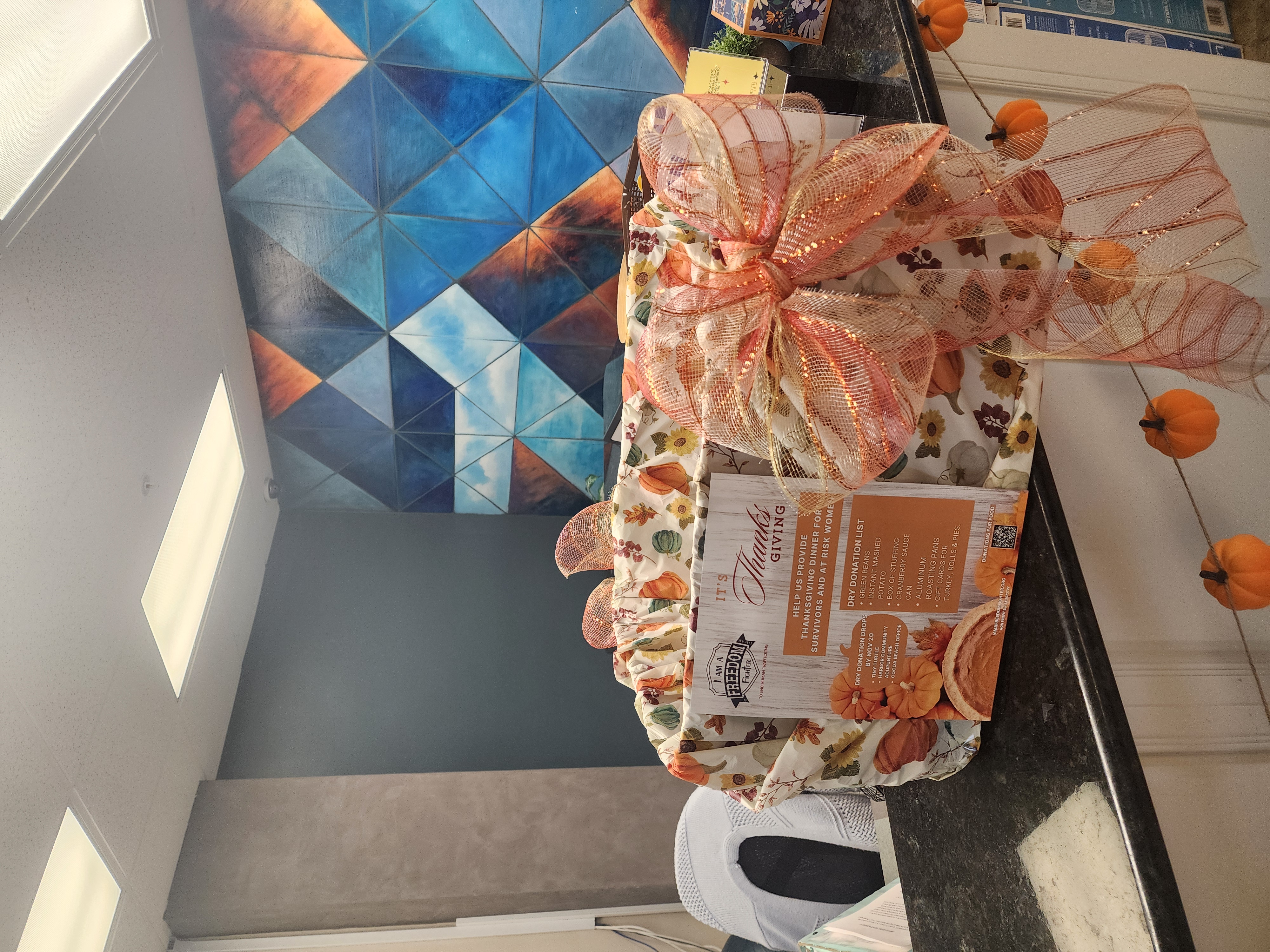 A Thanksgiving donation flyer and autumn-wrapped collection box with a large orange bow sit on a counter.