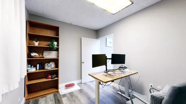 Reverse view of the office showing two monitor screens, tall wooden shelving, an open door and a gray chair.