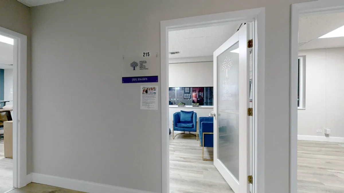 Front view of the Office 215 entrance, with its number beside an open frosted-glass door and blue chairs visible inside.