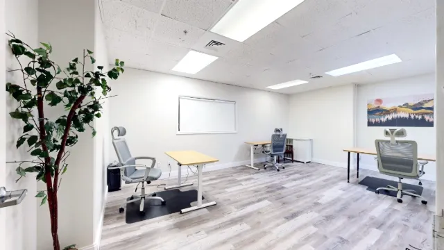 Wide doorway view of Office 229 with three desks, gray chairs, a shaded interior window and landscape artwork.