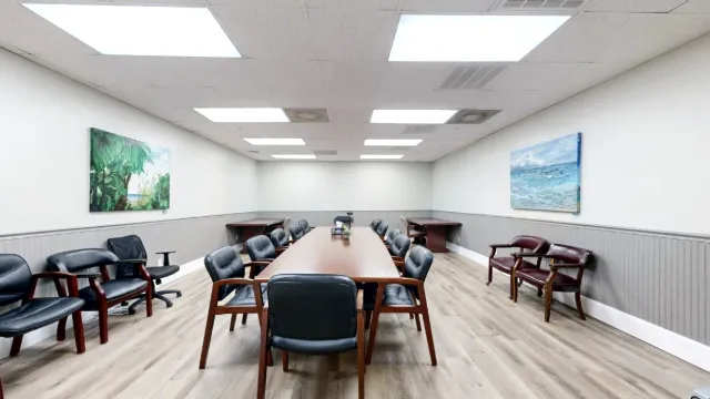 Centered view of the conference table with black padded chairs, extra wall seating and coastal artwork on both sides.