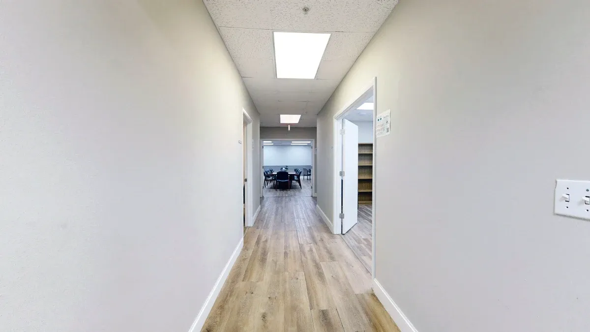 Hallway with wood-look flooring and open side doorways leading straight to the conference table visible at the far end.