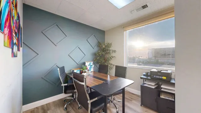 Office 203 with a wood desk, black chairs, geometric accent wall, large window, and printer cabinet.