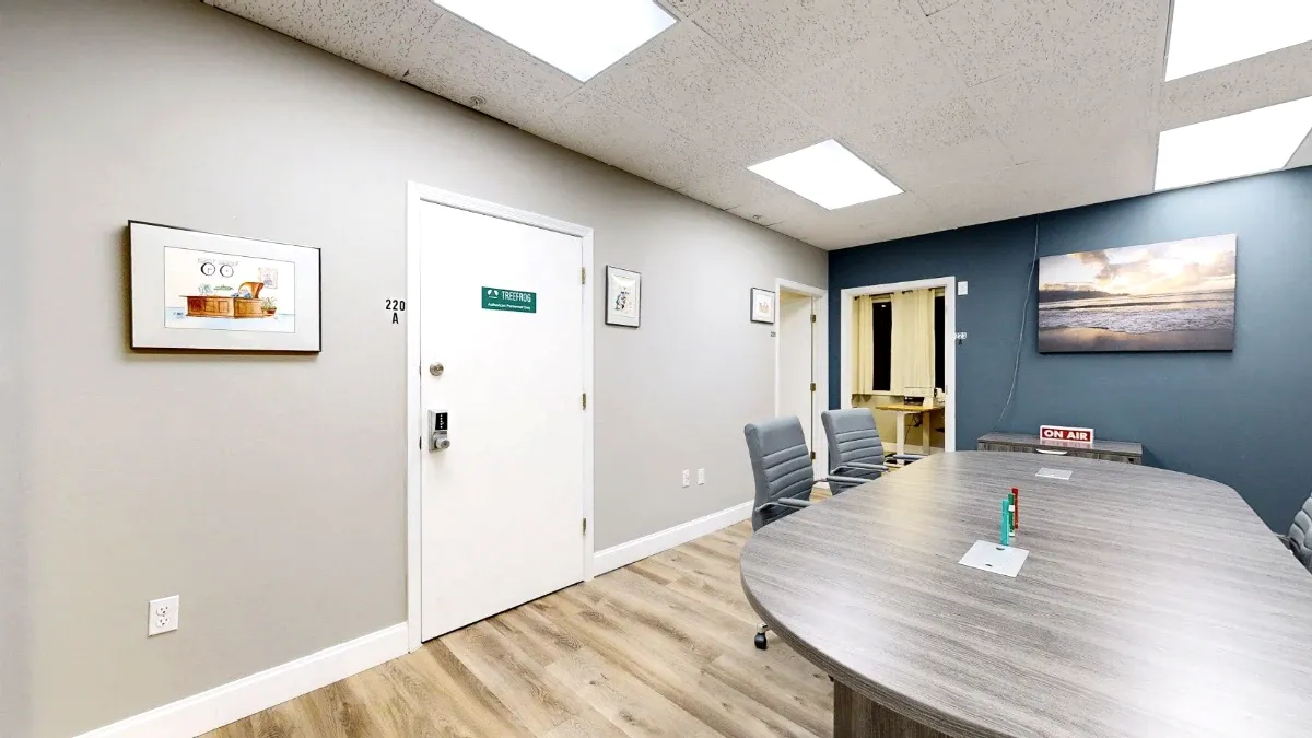 The broad gray tabletop fills the foreground, with rolling chairs, framed wall art and a blue accent wall behind it.