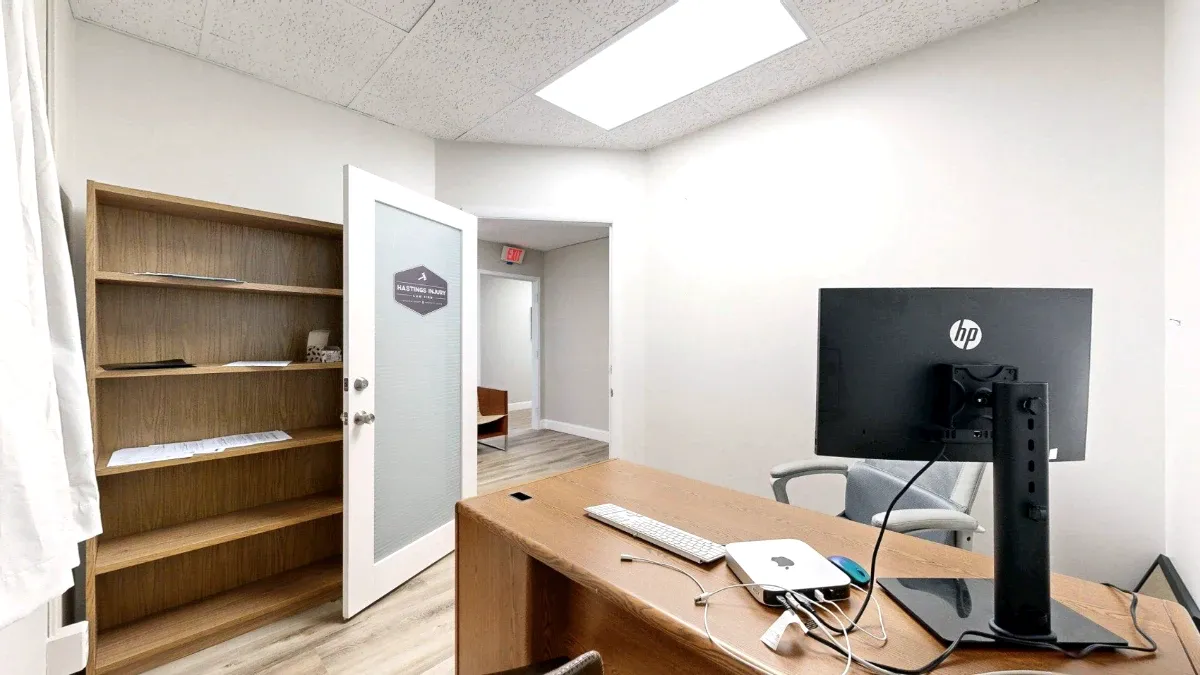 A wooden desk with a monitor fills the foreground, beside a tall bookcase and Office 221's open glass door.