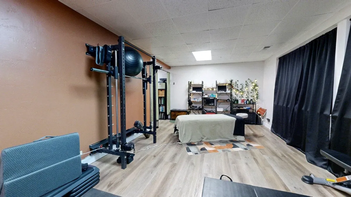 Reverse view of Office 227 with exercise equipment at left, a central massage table and supply shelves on the far wall.