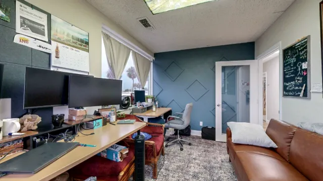 Private office with desks, dual monitors, a brown leather sofa, curtained windows, and a blue geometric accent wall.