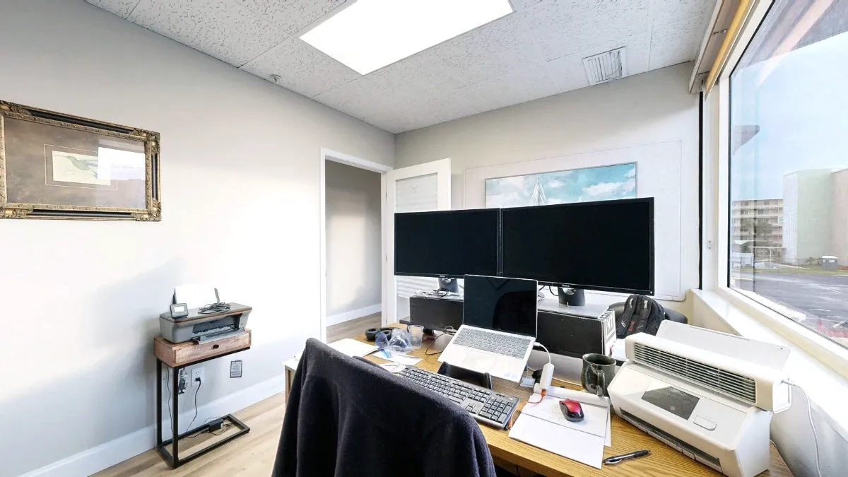 Office 201 workstation with two monitors, a laptop, a keyboard and a chair beside a large window.