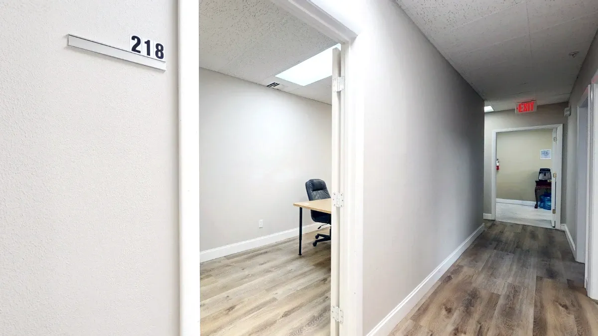 Office 218 sign beside an open doorway, with a desk and black chair visible inside and a hallway extending right.