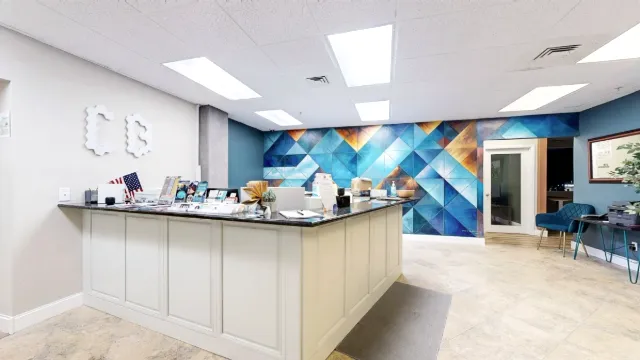 White paneled reception counter with brochures, a small American flag, and a blue geometric mural behind it.