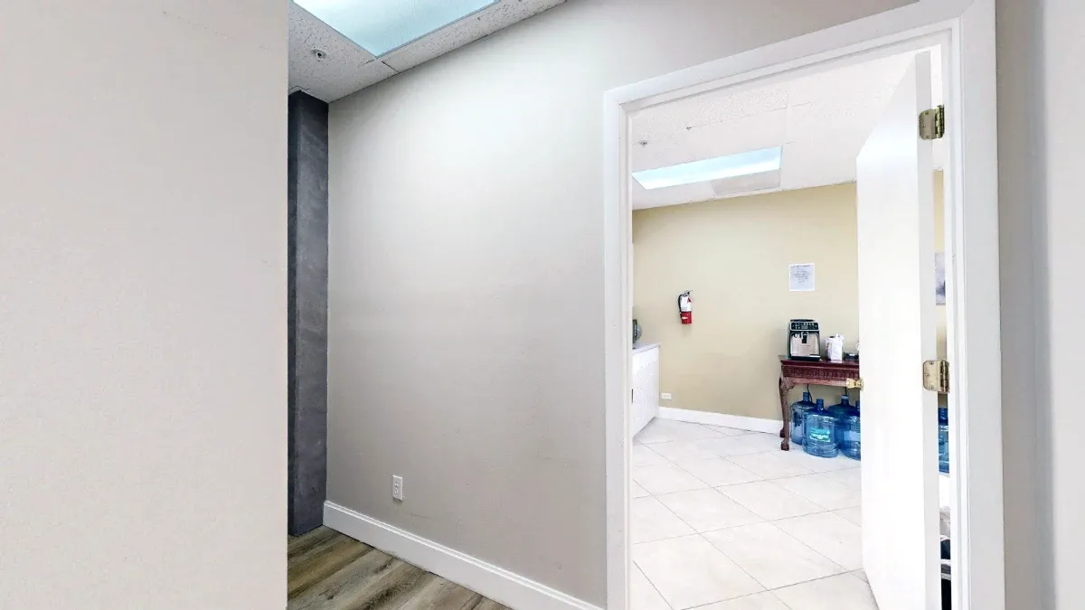 An open white door reveals the kitchenette's tiled floor and coffee table from the hallway.