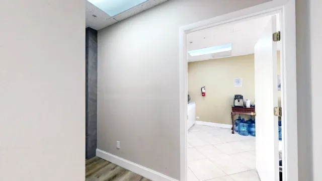 An open white door reveals the kitchenette's tiled floor and coffee table from the hallway.