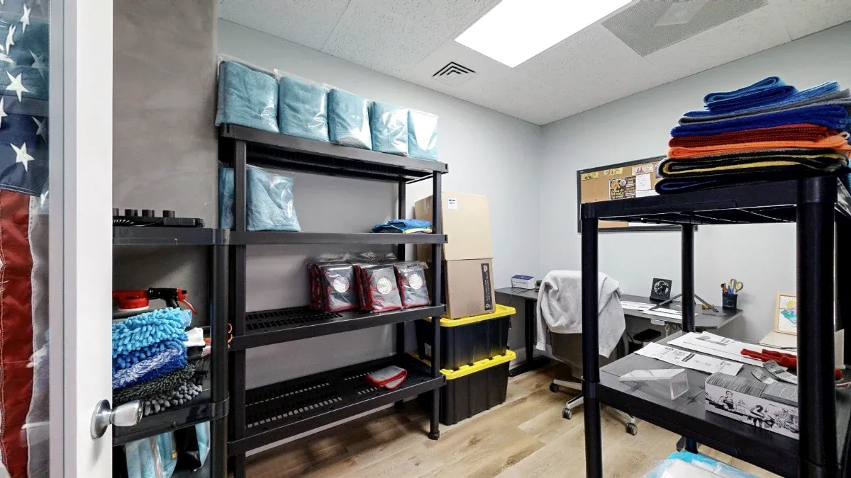 Inside Office 217, storage shelves and folded cloths frame a rear desk with a rolling chair and stacked bins.