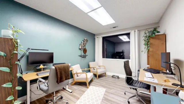 Two workstations flank Office 222A, with two cushioned guest chairs near a curtained window and plants beside a teal wall.