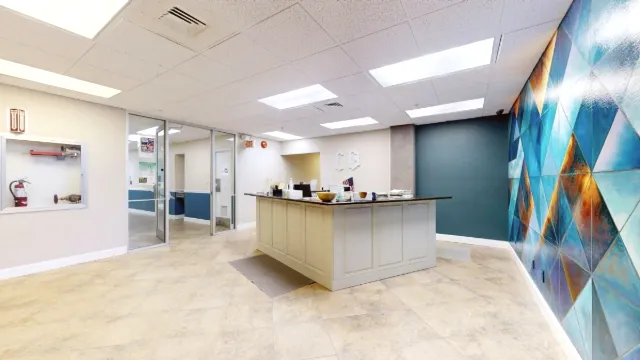 Blue and gold geometric mural dominates the right side of an open lobby view with the reception desk and glass entrance.