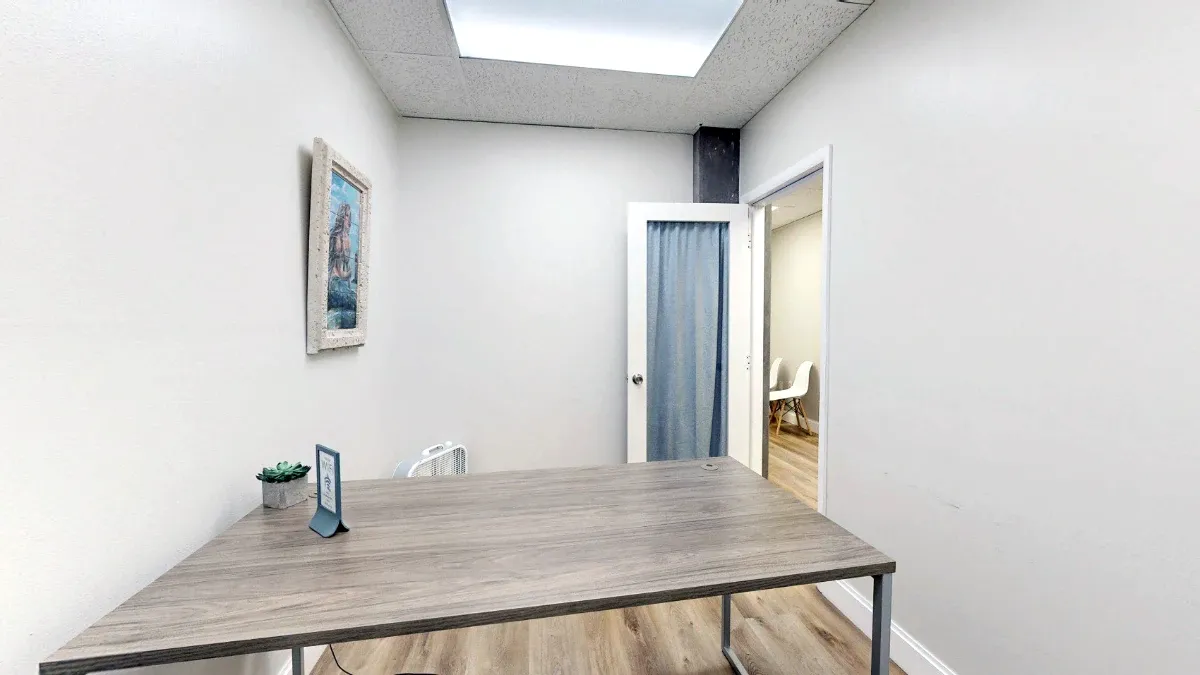 View across Office 217's desk toward an open door with a blue curtain, with a small plant and tabletop sign in the foreground.