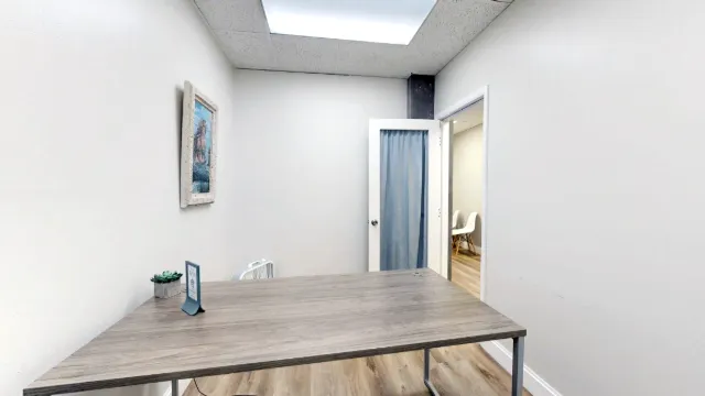 View across Office 217's desk toward an open door with a blue curtain, with a small plant and tabletop sign in the foreground.