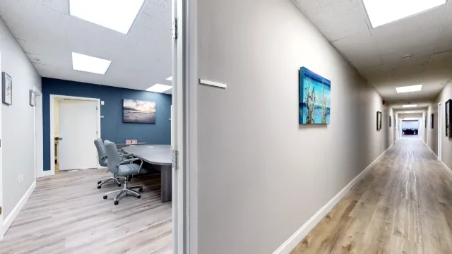 Open suite entrance reveals a conference table and gray chairs beside a long hallway lined with artwork.
