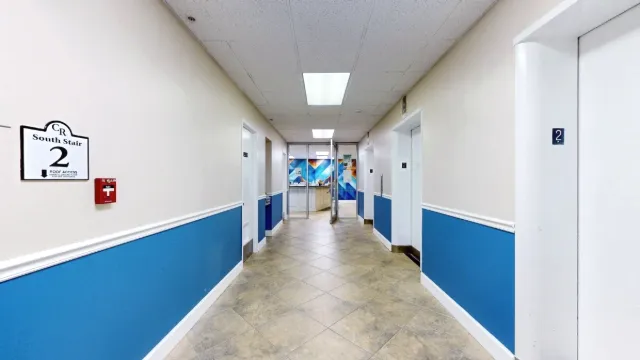 Blue-and-white elevator corridor leading through open glass doors to the reception desk and colorful mural.