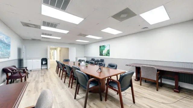 Diagonal view across the meeting table toward the open entrance, with side tables and extra chairs along the walls.