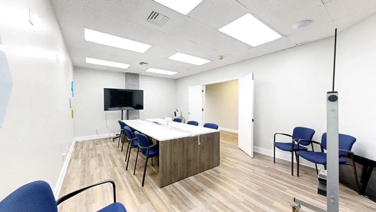 Wide interior view of The Canaveral with a central meeting table, blue chairs, a display and open double doors.
