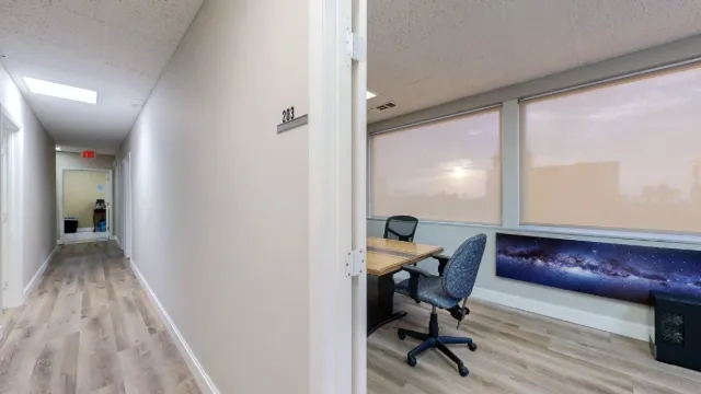 Hallway outside office 203, looking through the doorway toward shaded windows, a rolling chair, and galaxy artwork.
