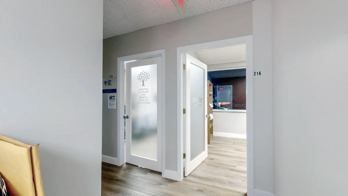 Hallway view of office 216 with its frosted-glass door open beside a neighboring office entrance.