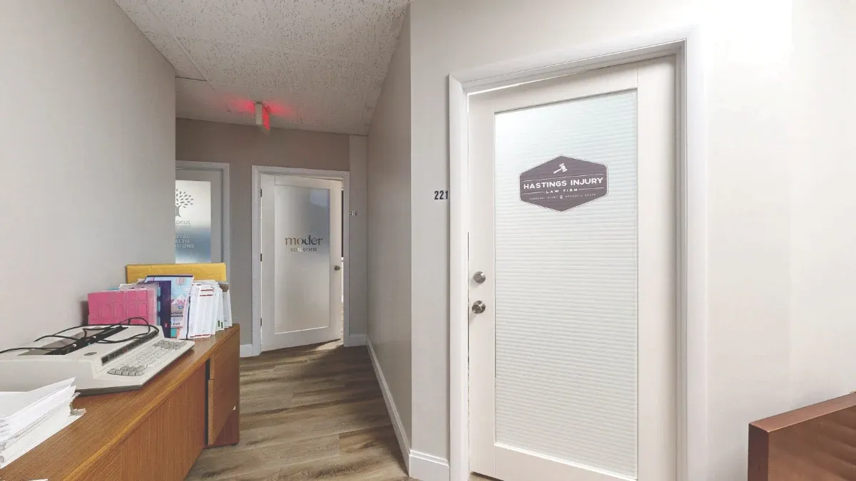 The closed glass door of Office 221 has blinds and a business sign, with a wooden cabinet along the opposite hallway wall.