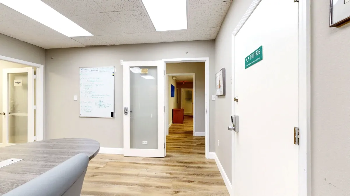 A whiteboard hangs beside an open frosted-glass door leading to a hallway, with the meeting table cropped at left.