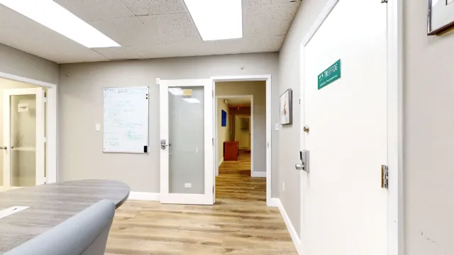A whiteboard hangs beside an open frosted-glass door leading to a hallway, with the meeting table cropped at left.