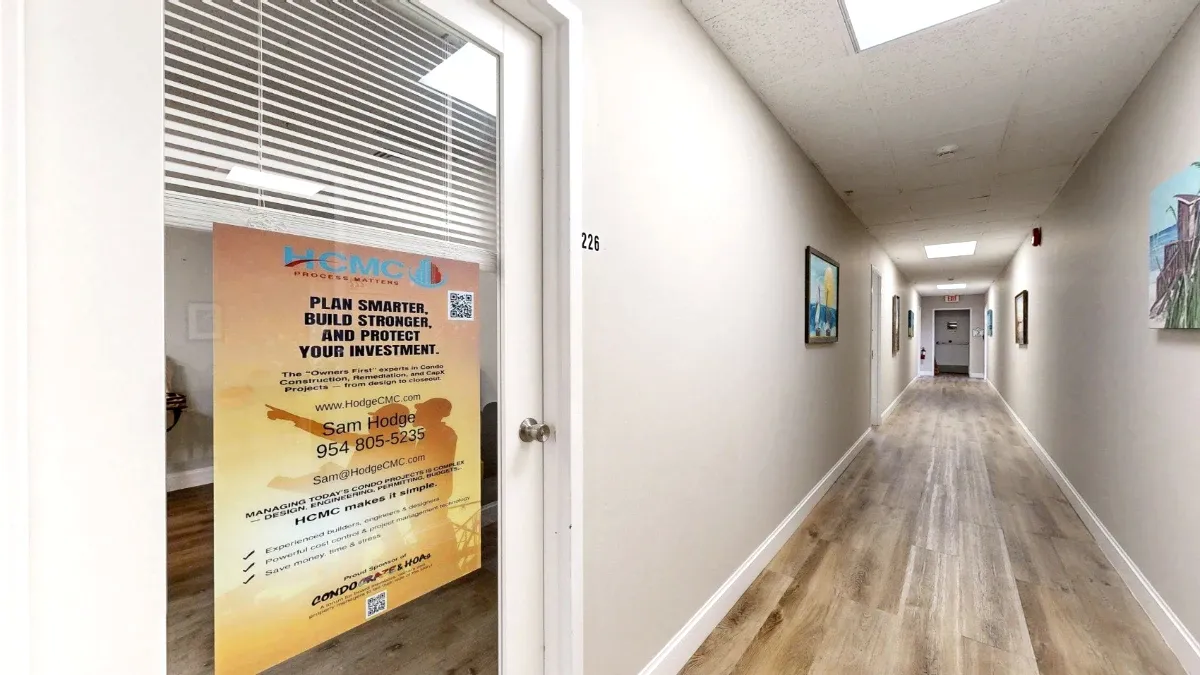Office 226's glass door with blinds and an orange sign beside a long hallway with artwork and wood-look flooring.