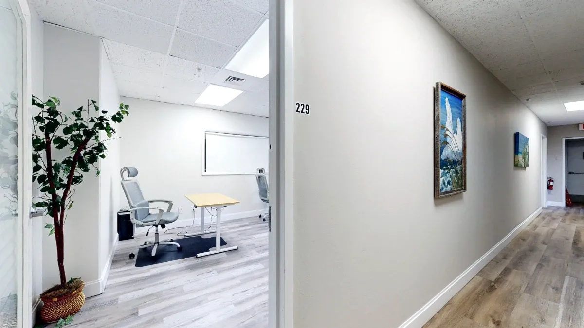 Hallway view into Office 229 shows the unit number, a potted tree, a light-wood desk and a gray office chair.