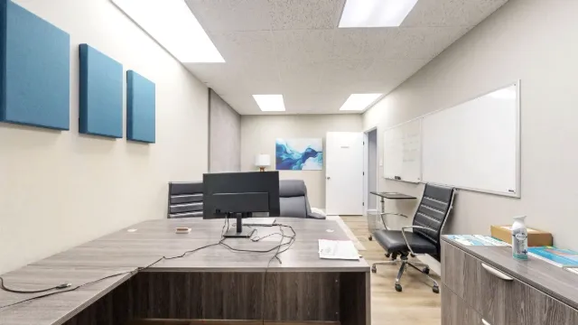 View across a large desk and monitor toward Office 224A's entrance, with whiteboards and a storage cabinet on the right.