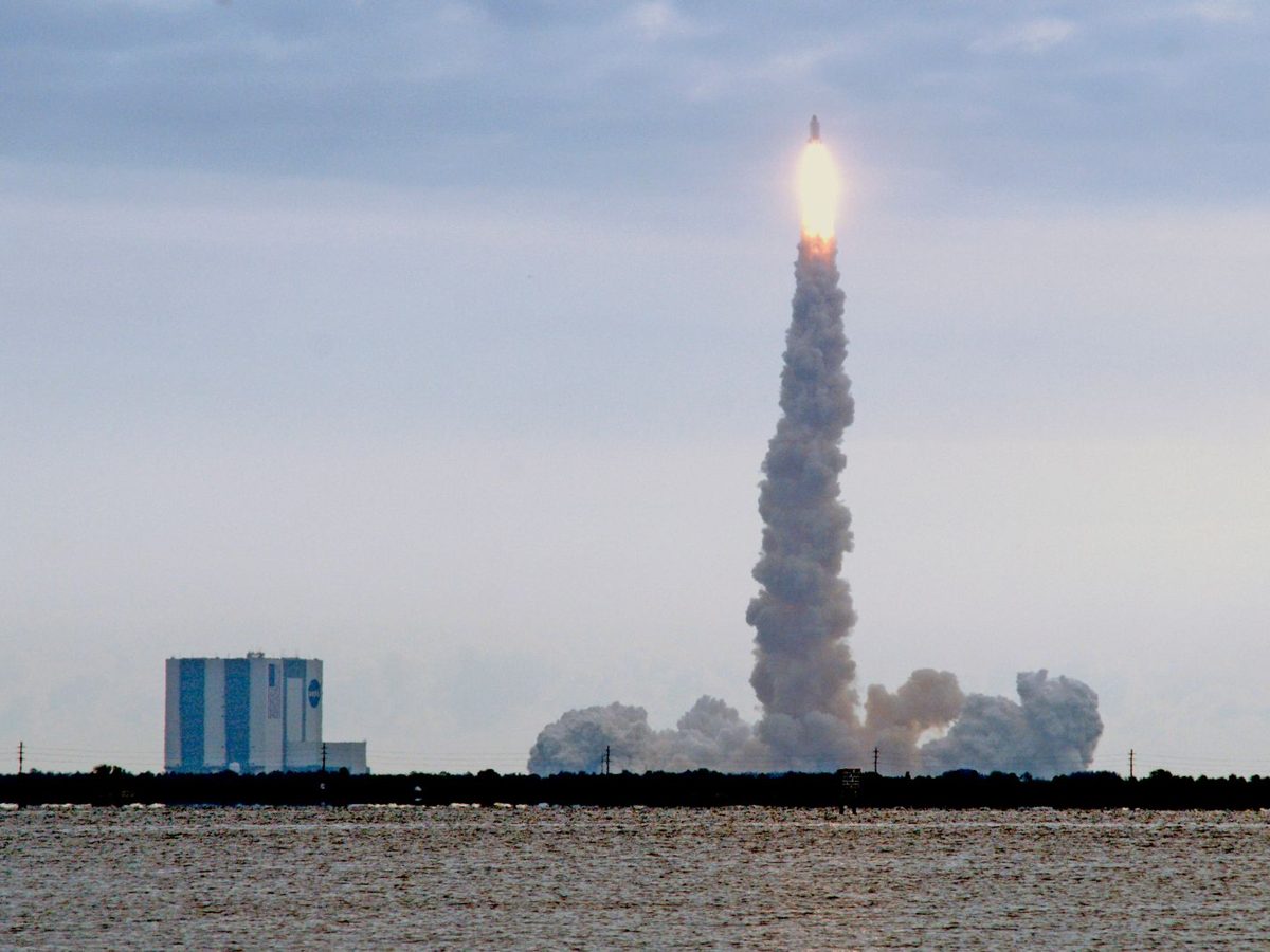 Coastal editorial illustration of a satellite, launch trajectory and engineering plans